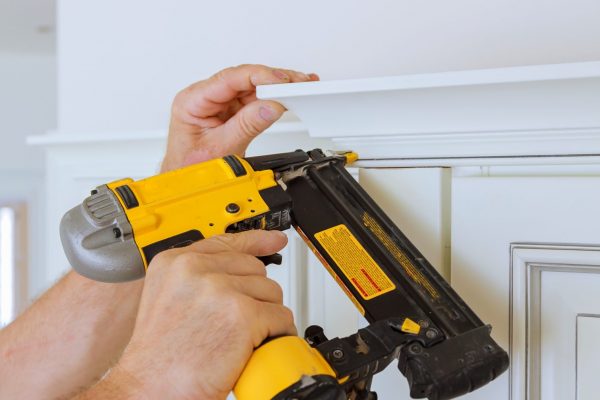 Carpenter brad using nail gun to Crown Moulding on kitchen cabinets framing trim, with the warning label that all power tools have on them shown illustrating safety concept